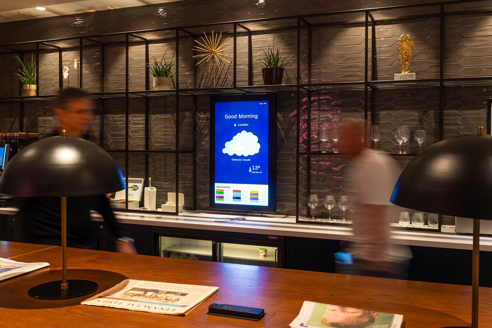 Residents in a first-floor coffee and amenity area, with a portrait Abode screen showing building and weather information.