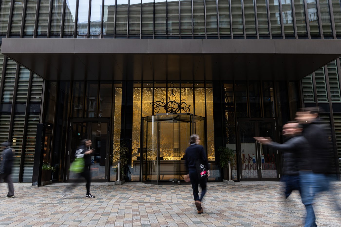Residents walking into the entrance of a premium London residential building at dusk, through a bronze-framed revolving door.