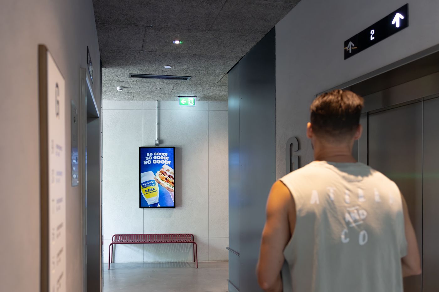 A resident walking towards the lifts in a residential lobby, passing a lit Abode screen.