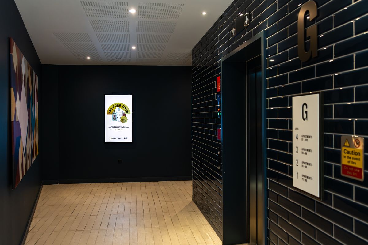 A navy brick lobby with a large geometric mural and a portrait Abode screen running a brand campaign.