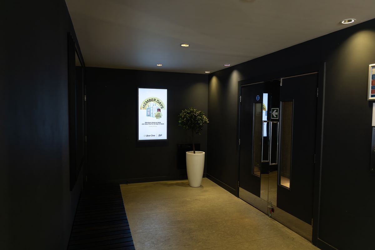 A dark residential corridor leading to glazed doors, with a lit portrait Abode screen alongside.