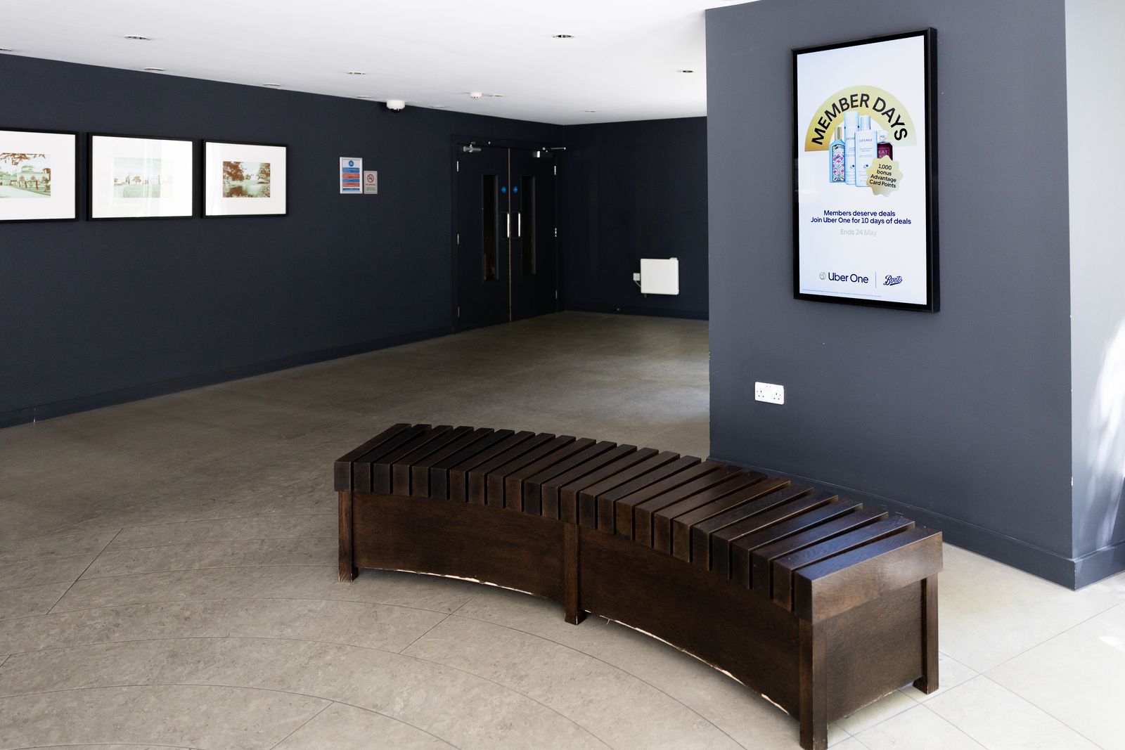 A wide residential lobby with a curved timber bench and framed prints; an Abode screen at the far end.