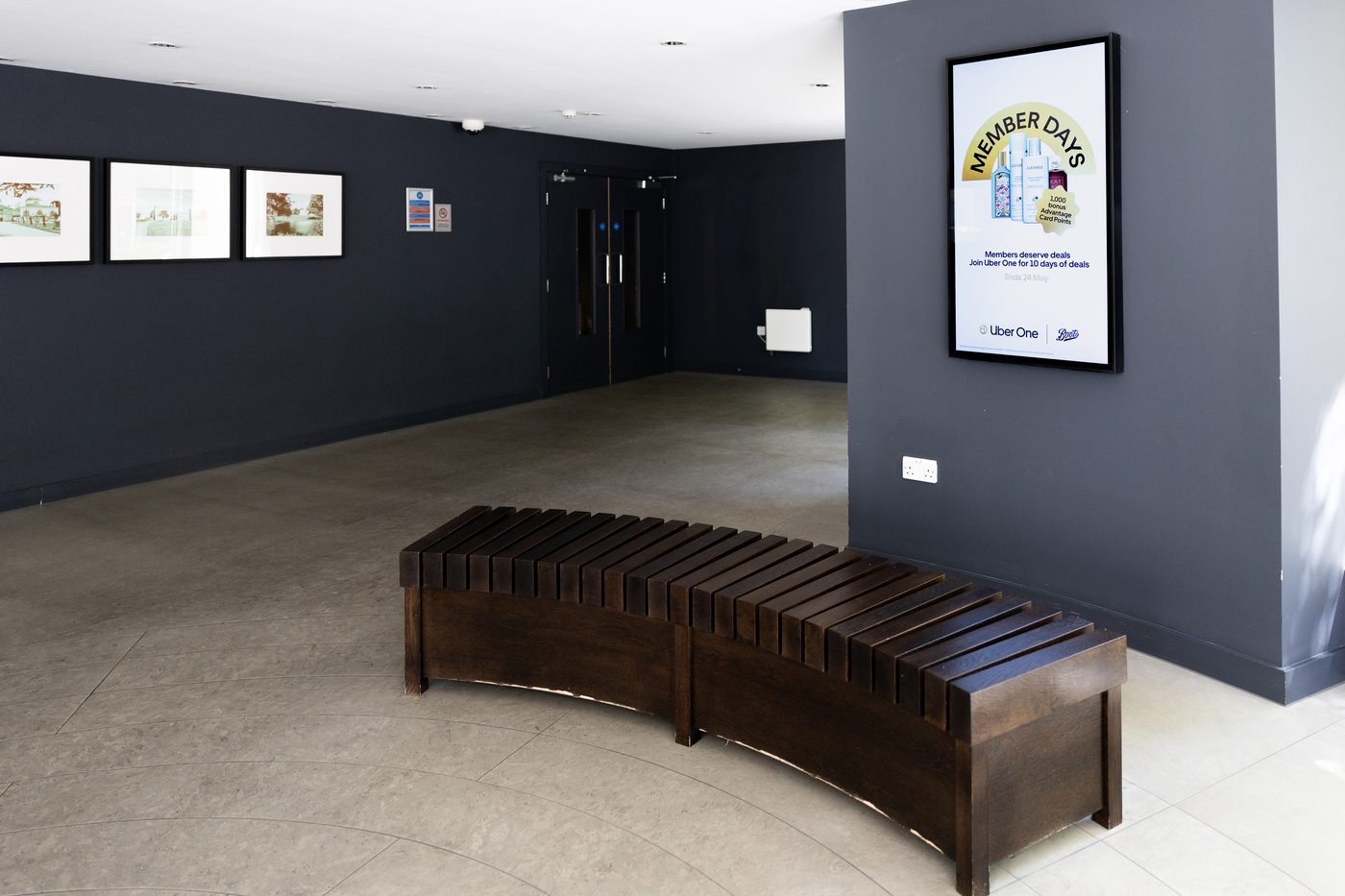 A navy glazed-brick lobby with two portrait Abode screens beside the ground-floor wayfinding.